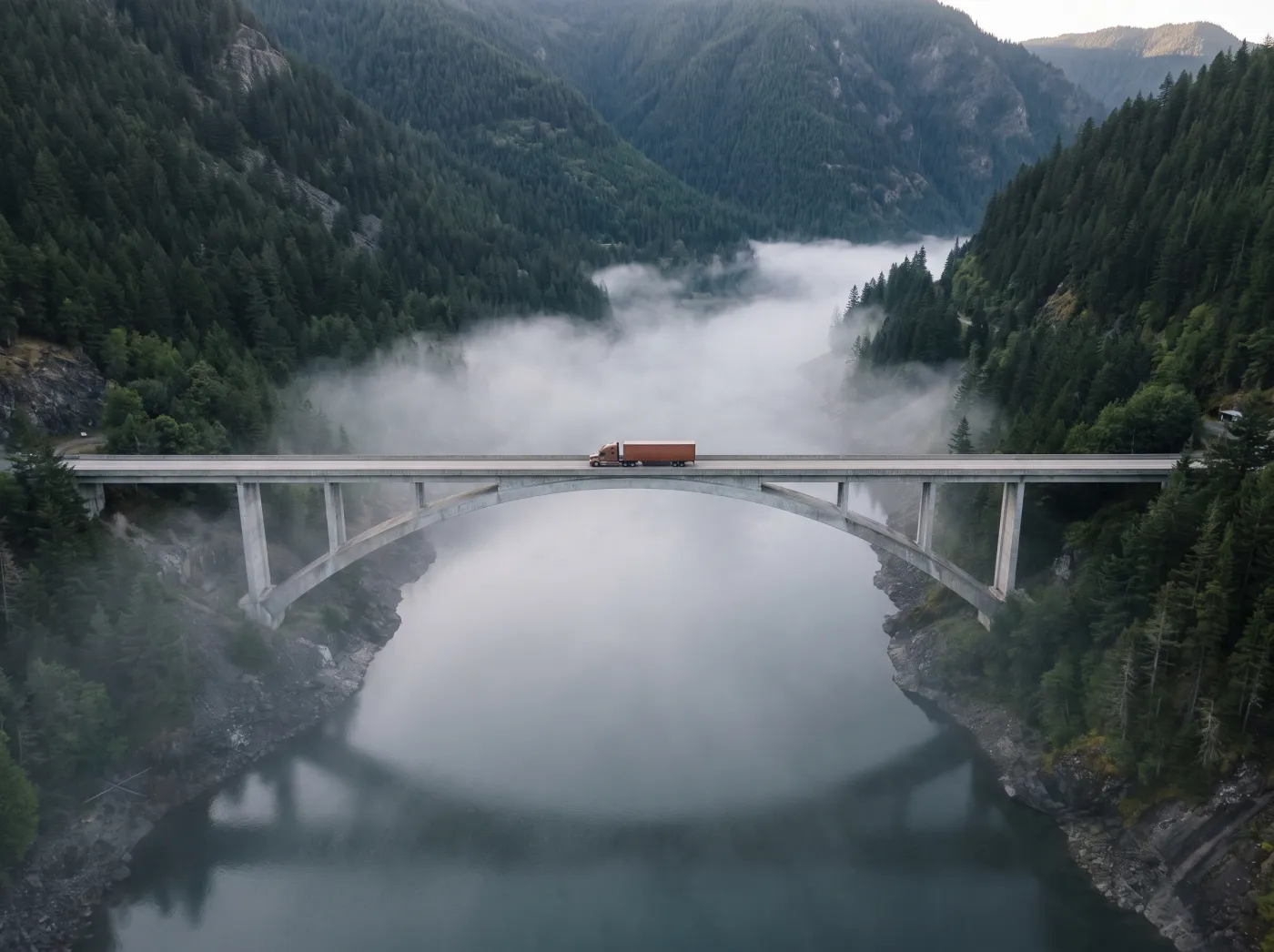 A single lorry with an orange trailer on a long road through a misty valley